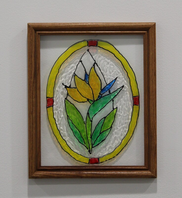 Stained glass art with a yellow flower and green leaves in a wooden frame.
