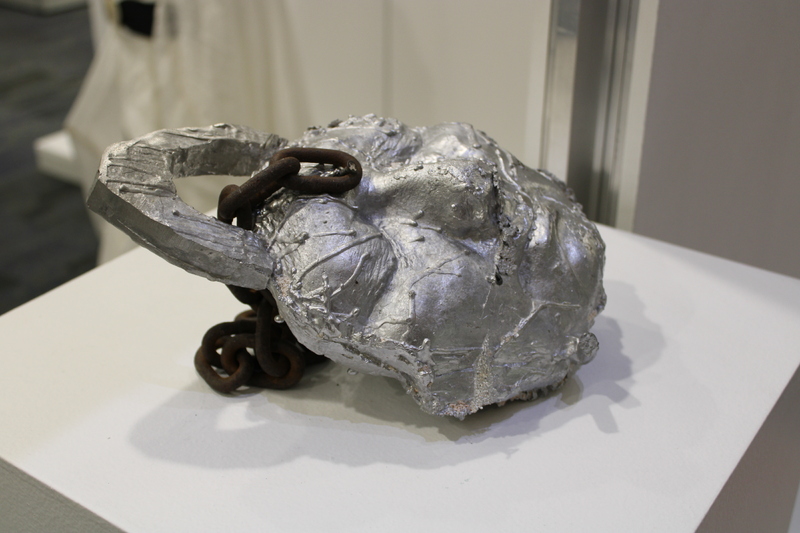 Metallic sculpture resembling an abstract face with rusty chain embedded.
