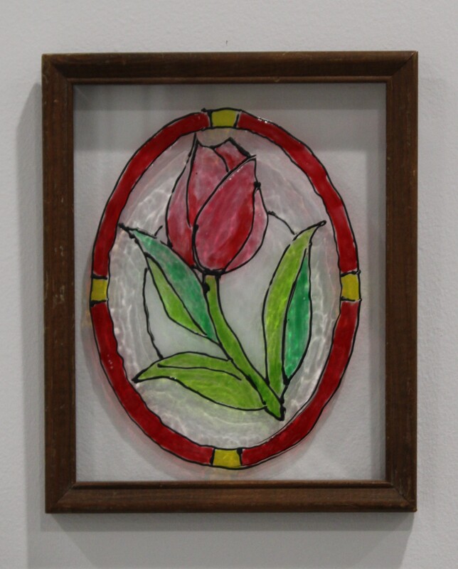 Stained glass panel of a red tulip with green leaves encircled by a red ring.