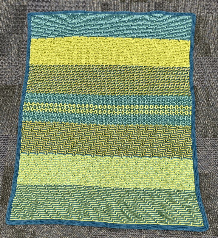 Artist: Lisa Louis. 60 by 40-inch mosaic crochet afghan. Afghan crocheted in intricate geometric patterns in hues of green and blue.