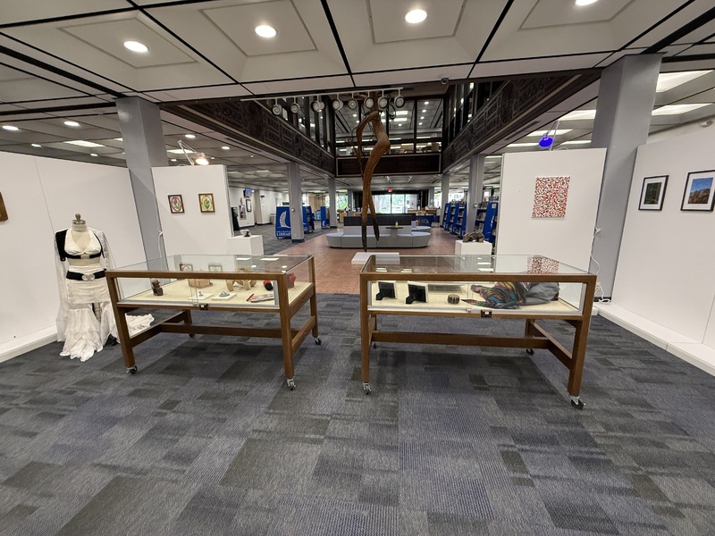 Art exhibition space with various artworks on walls, pedestals, and tables.