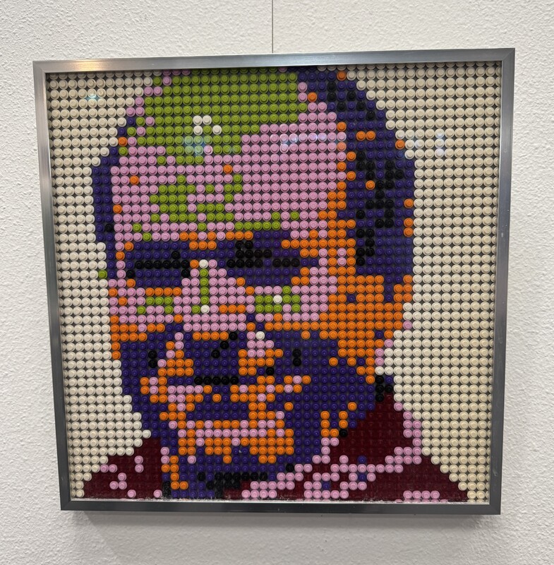 Artist: Ruby Mehrubeoglu. 16 by 16-inch framed Lego piece. Lego 1x1 plate round dots attached to a background plate, the dots are arranged to create a portrait.