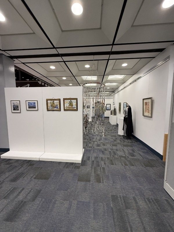 Art exhibition space with various artworks on walls, pedestals, and tables.
