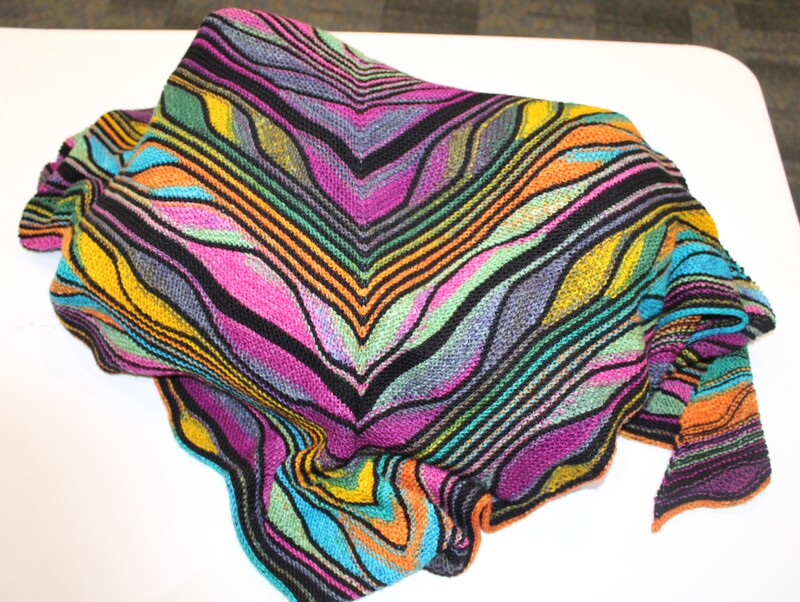 A colorful knitted fabric with V-shaped stripes in black, pink, purple, yellow, green, blue, and orange draped on a white surface.