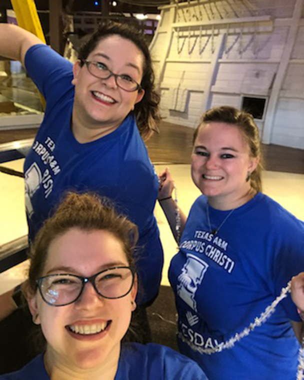 Color photograph of three people dressed in blue, smiling at the camera