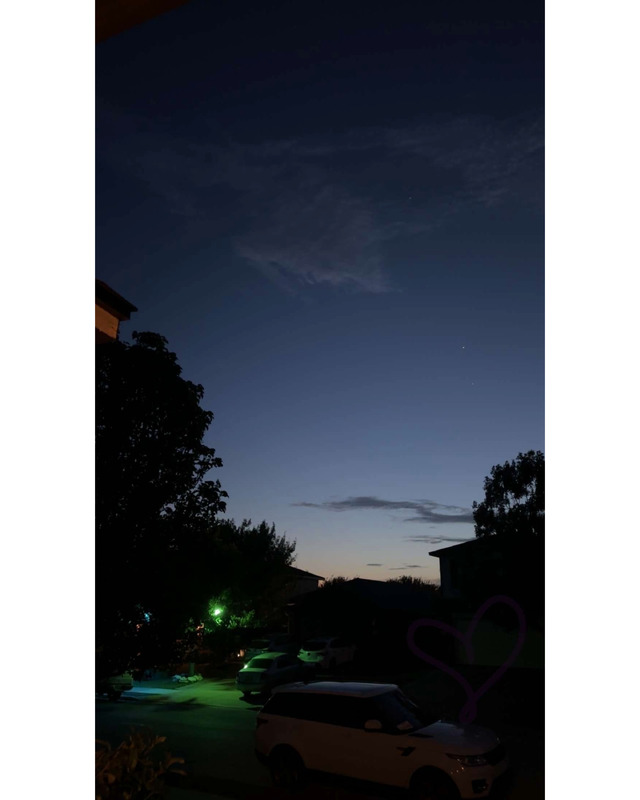 Twilight scene featuring a clear sky with scattered clouds, parked cars in a residential area, and a green light illuminating the foreground.