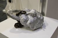 Metallic sculpture resembling an abstract face with rusty chain embedded.
