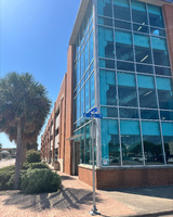 Building with glass windows, a street sign, and palm trees against a clear sky.