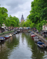 color photograph of a river lined with boats and trees, a large steepled building is in the background