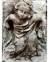 Stone sculpture of a winged figure with flowing robes and wavy hair.