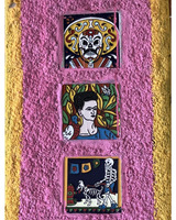 Three colorful ceramic tiles on a pink wall: a decorative skull, a portrait of a woman reminiscent of Frida Kahlo, and a skeleton walking a dog.