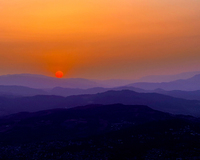 A vibrant red sun sets over layered purple and orange mountains, creating a tranquil gradient sky.