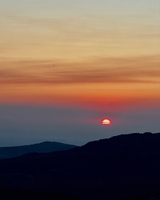 Sunset over dark mountain silhouettes, with vibrant orange and red hues in the sky, creating a gradient effect.