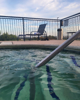 Close view of a hot tub with clear water, a black lounge chair with a towel, and a pair of flip-flops nearby, set against a distant landscape and cloudy sky.