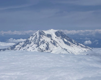 Snow-covered mountain peak above clouds and beneath a blue sky.