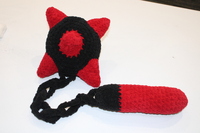 Crocheted toy flail with a red mace and black handle on a white surface.
