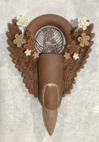 Artist: Leandra Urrutia. 13 by 7 by 3-inch ceramic and wire sculpture. The sculpted piece includes a fingertip with sharpened nail flanked by wings and flowers. The sculpture has a circular top with a delicate latticed structure in the center.