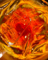 Close-up of colorful liquid with ice, featuring vibrant red, orange, and yellow hues, enhanced by reflections and bubbles.