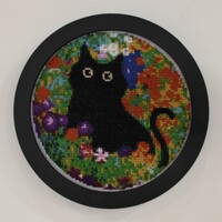 Embroidery hoop with black cat cross-stitch art in colorful floral background.
