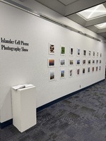 Interior view of a photographic exhibition titled "Islander Cell Phone Photography Show," featuring framed photographs on white walls.