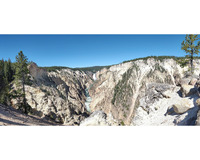 A distant waterfall cuts through tree topped rocky mountains. The falls are centered in the frame and extend down towards the viewer. The sides of the mountain and the foreground are bare rock. The image is bound a white border at the top and bottom of the frame.