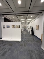 Art exhibition space with various artworks on walls, pedestals, and tables.