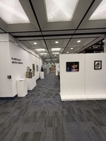 Art exhibition space with various artworks on walls, pedestals, and tables.
