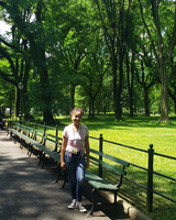 color photograph of a figure standing near benches and a fence in a wooded park