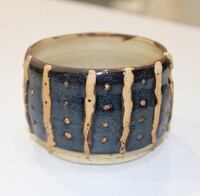 A handcrafted ceramic cup with slate-blue glaze, beige vertical lines, and dot patterns.
