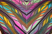 A colorful knitted fabric with V-shaped stripes in black, pink, purple, yellow, green, blue, and orange draped on a white surface.
