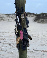 A wooden post on a sandy beach covered with various shoes.