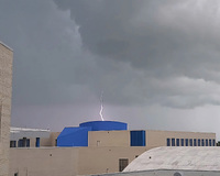 Lightning strikes a blue-roofed building under dark storm clouds.