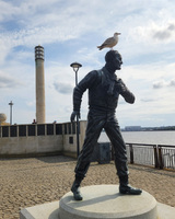 Bronze statue with a seagull on its head near a waterfront.