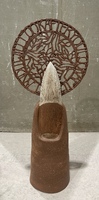 Artist: Leandra Urrutia. 12 by 5 by 2.75-inch ceramic sculpture. An upright fingertip with sharpened nail is topped with a delicate circular ceramic disc with patterns and script.