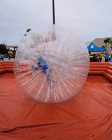 A clear inflatable zorb ball with a person inside, placed within an orange inflatable structure, against a cloudy sky and a distant blue tent reading "A&M-Corpus Christi."