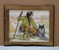 Framed cross stitch of a person with a staff sitting beside a wolf, set against a muted landscape.
