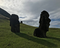 Two large stone Moai sculptures on a green hillside under a partly cloudy sky.
