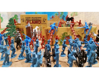 A colorful diorama of toy soldiers depicting a battle at the Alamo, featuring blue soldiers in formation, red soldiers climbing, and a cannon in the foreground.