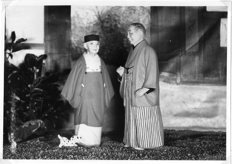 Black-and-white photo of two dolls in traditional Japanese attire with a small toy dog.