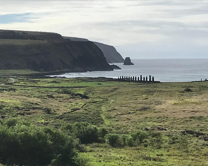 Coastal landscape with Moai statues in the distance and ocean background.