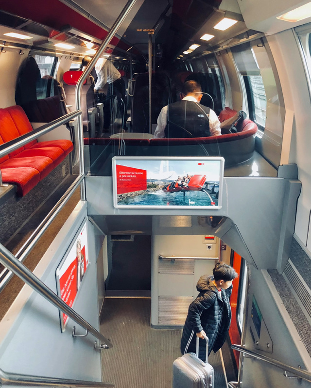 Interior of a double-decker train with passengers and a young boy holding a suitcase near the door.
