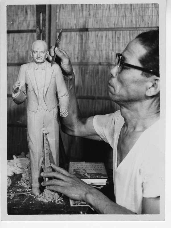 Man sculpting a detailed figurine of a man in a suit.