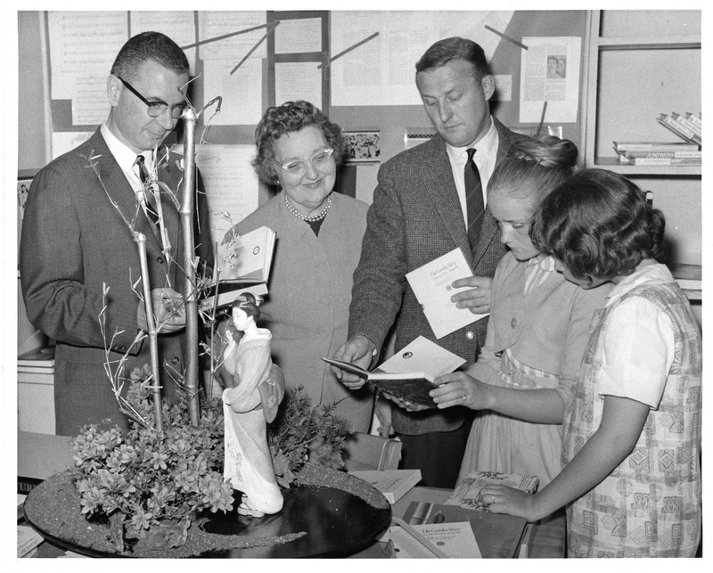 Group of adults and children examining a display with a model tree and a figurine.