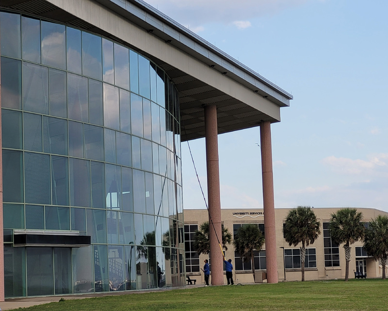A building with a curved glass facade next to the "University Services" building and palm trees.