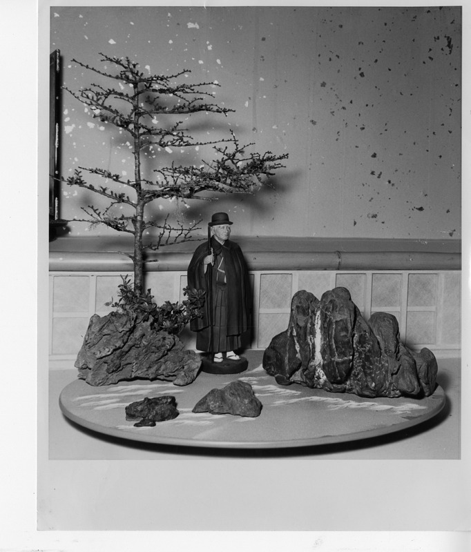 A model tree, a figurine in traditional attire, and rocks on a round base.