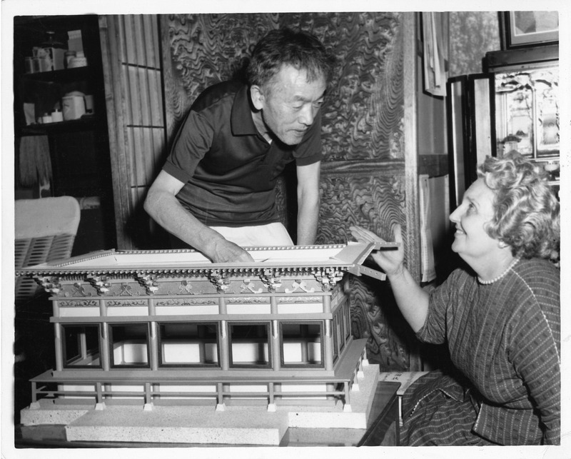 Two people examine an architectural model of a traditional Asian building.