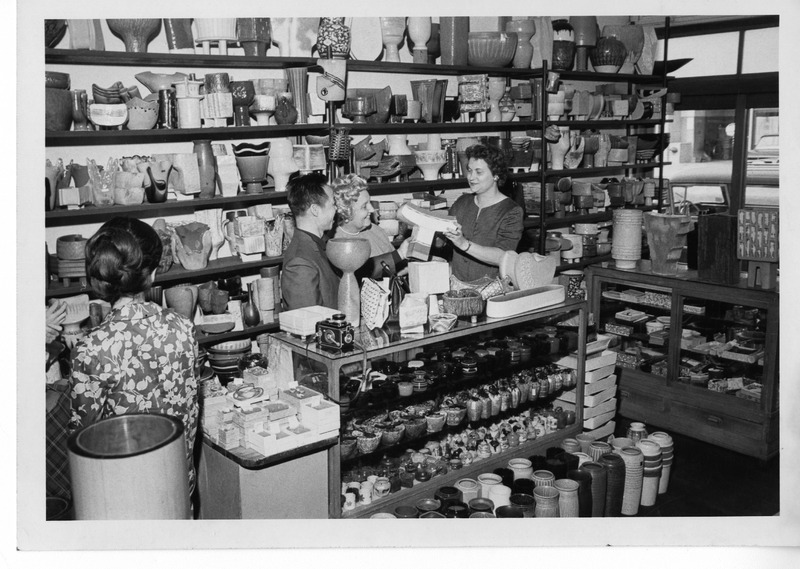 Store interior with shelves of pottery; a woman assists customers at the counter.