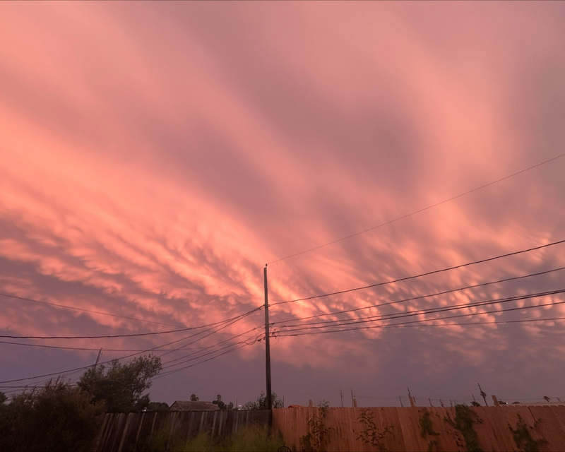 Pink and orange sunset sky with wavy clouds and power lines.
