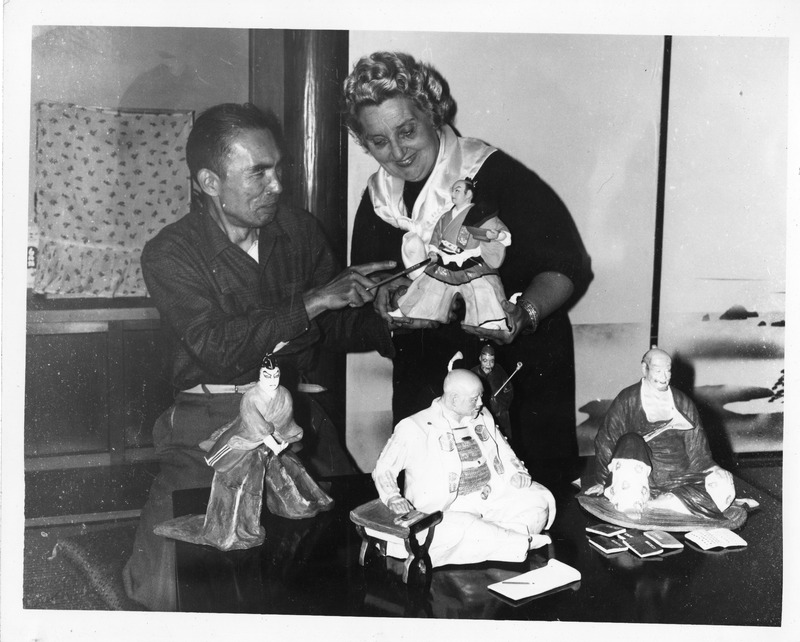 Two people examining traditional Japanese dolls on a table.