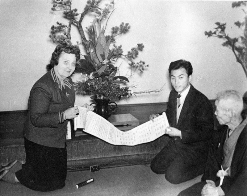 Three people kneeling on the floor examine a scroll with text.